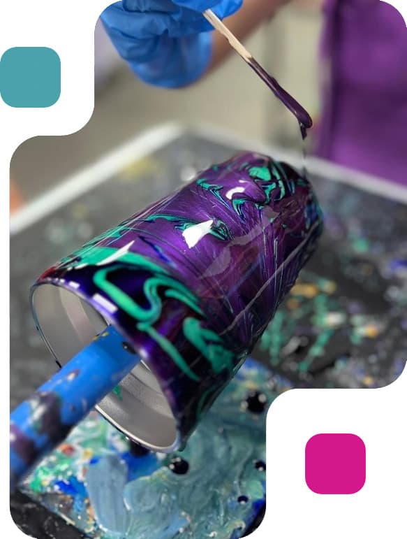 A guest pouring vibrant teal and purple paint over a tumbler at an ATL Fluid Art corporate event